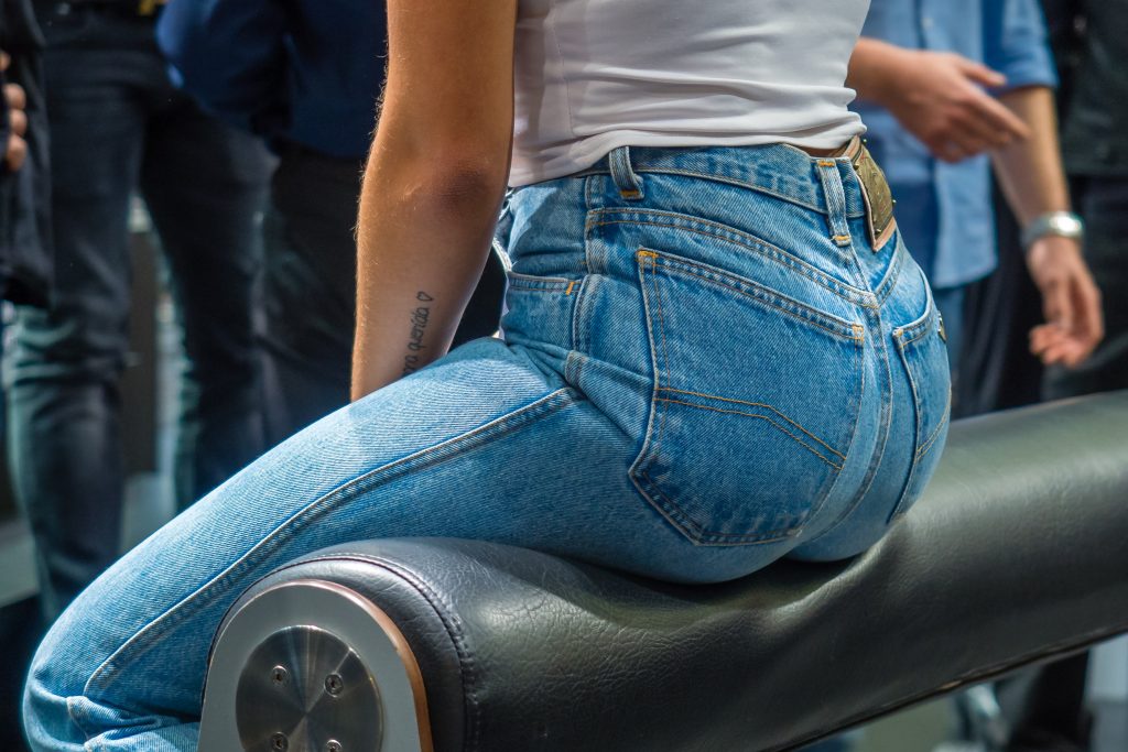 Das Bild zeigt den Hintern einer Frau sitzend in einer Jeans auf einem Balken.