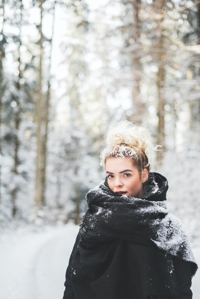 Das Bild zeigt eine junge Frau im Schnee im Wald.